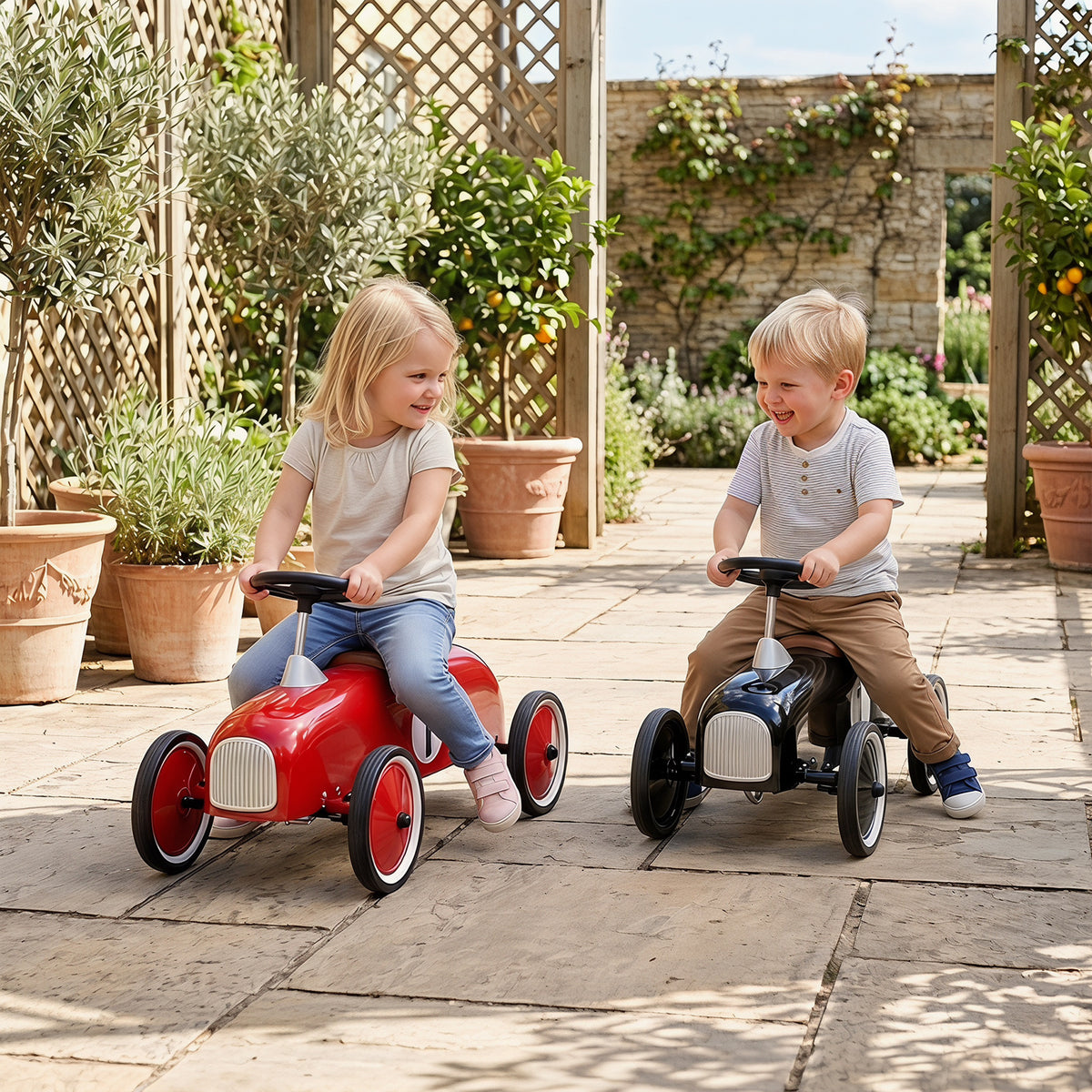 Two children, a boy and a girl, ride red and black push and pedal ride on toys outside