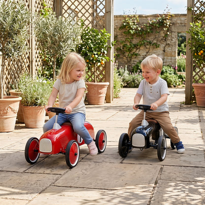 Two children, a boy and a girl, ride red and black push and pedal ride on toys outside