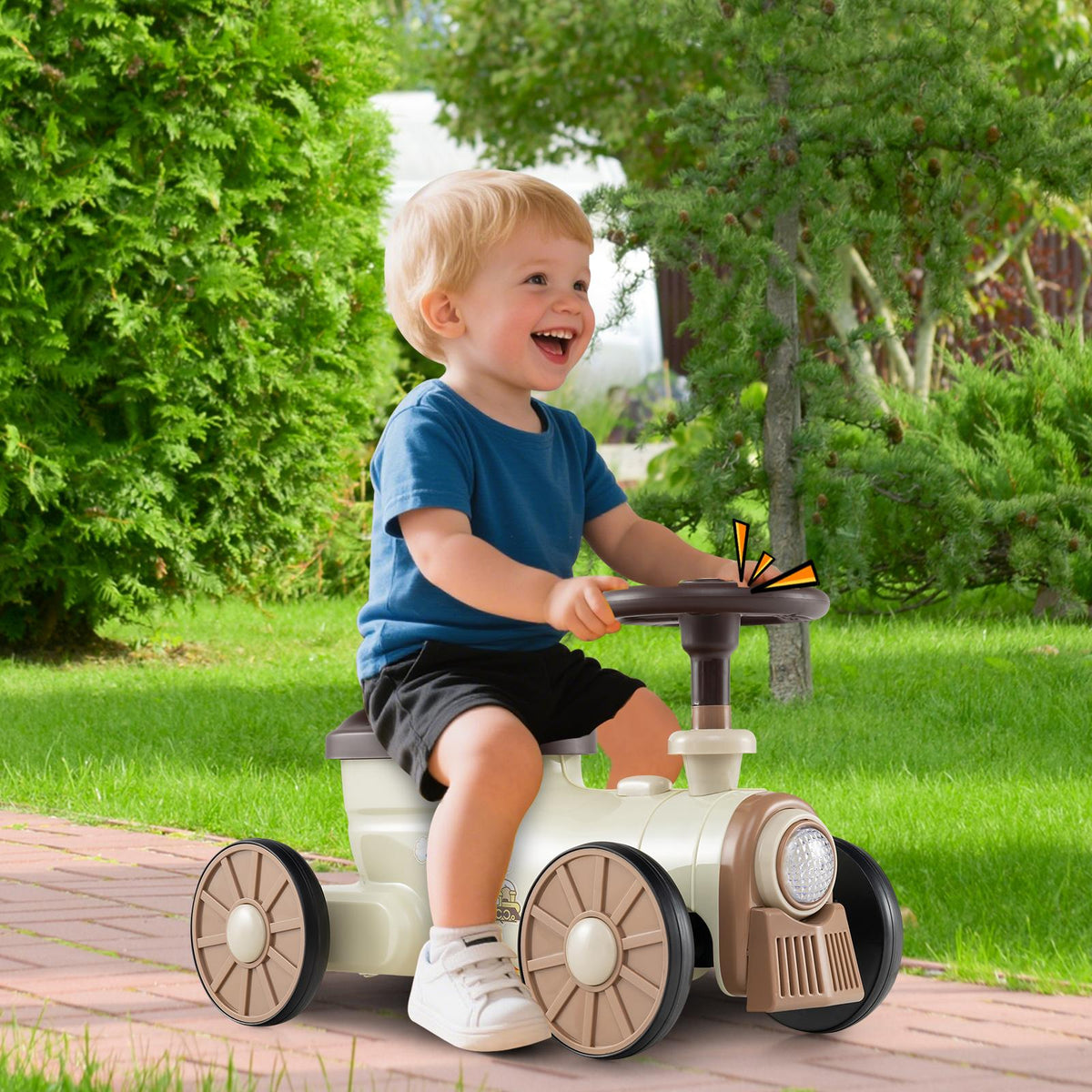 Happy toddler boy riding the beige push car train on a paved garden path