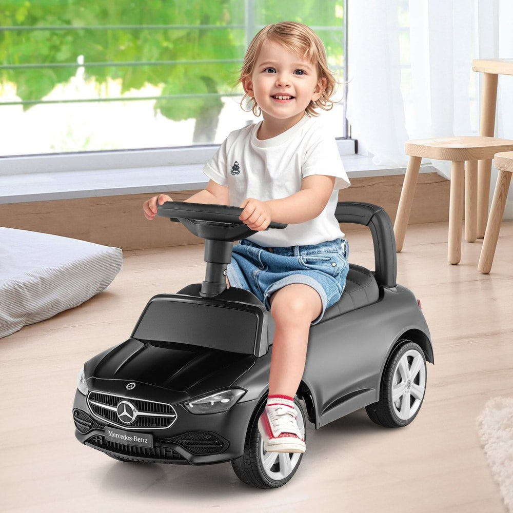 A smiling baby girl sitting on the black push and pedal ride on toy, indoors
