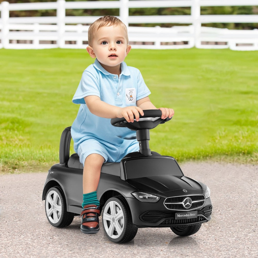 A happy baby boy sitting on the black push and pedal ride on toy, outdoors