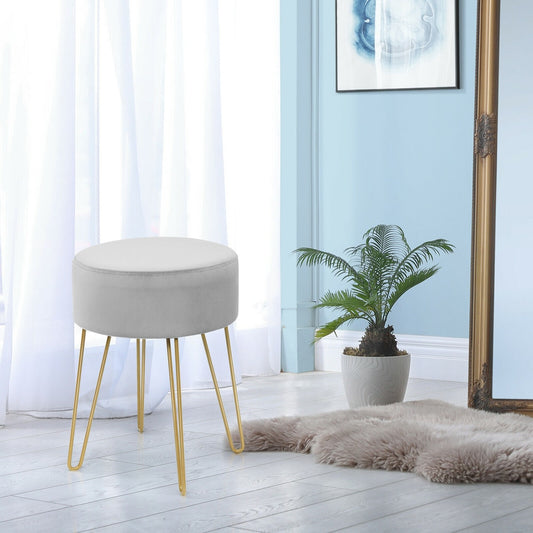 Grey velvet footstool with gold hairpin legs in a bright room with a plant