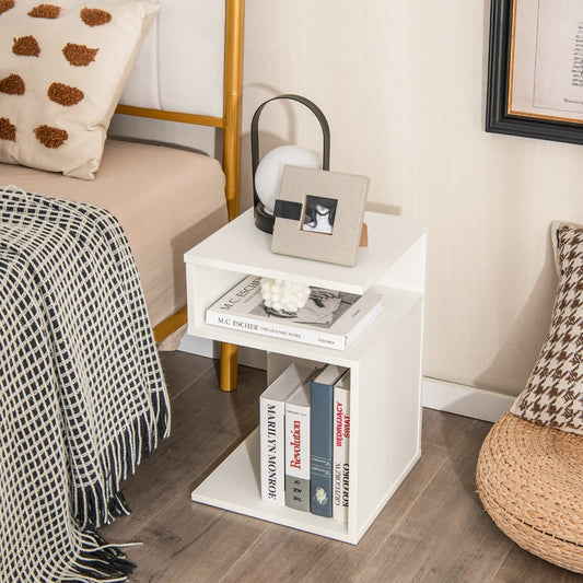 White S-shaped end table with two open shelves, placed beside a bed with books and a lamp