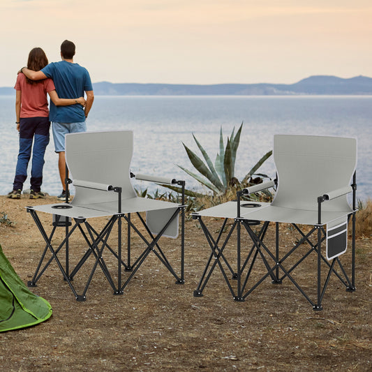 Two grey oversized camping chairs with side tables set up outdoors by the water