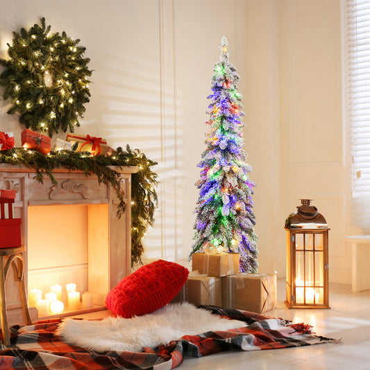 The snow-flocked slim pencil Christmas tree with colourful lights is set up in a cosy living room next to a fireplace