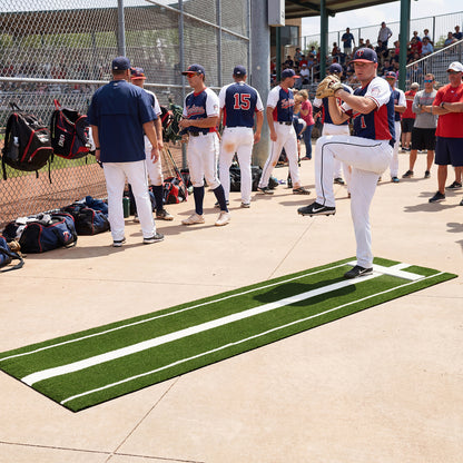 A baseball pitcher practices on a green artificial turf training aid at a baseball field