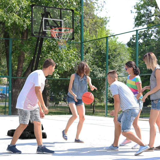 A group of young people playing basketball with the adjustable hoop and stand outdoors