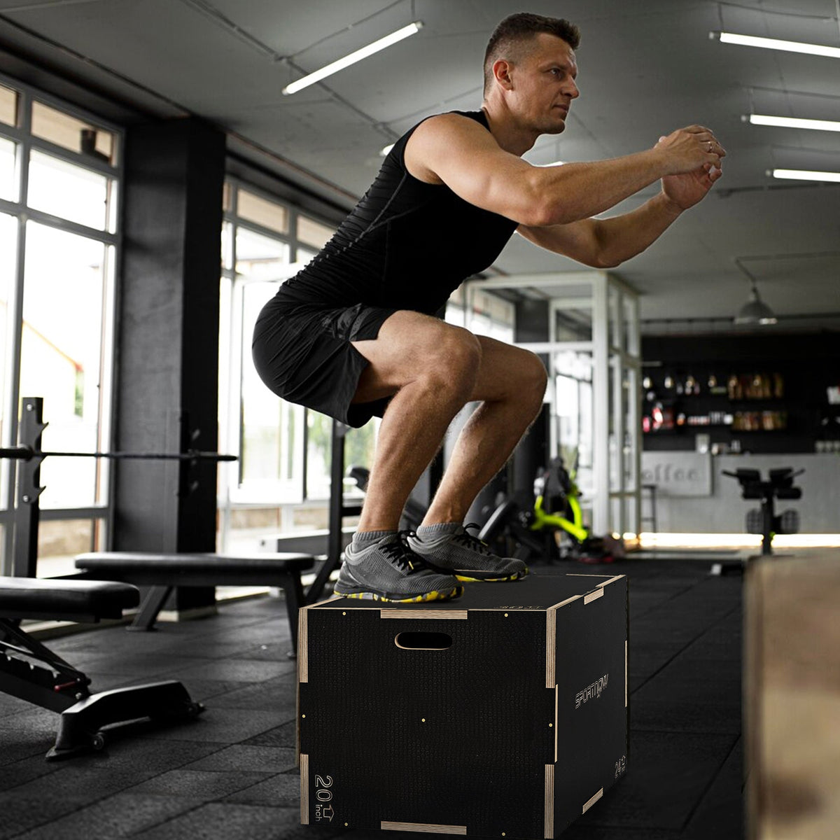 A man performing a box jump on the wooden plyometric box in a gym setting