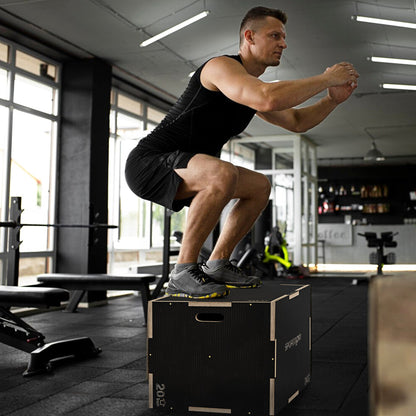 A man performing a box jump on the wooden plyometric box in a gym setting