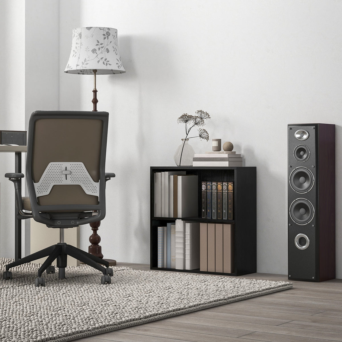 The low bookcase placed in a home office setting next to a desk chair and a tall speaker