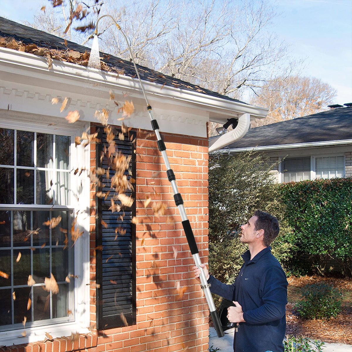 the telescoping wand spraying water to clear leaves from a residential roof gutter