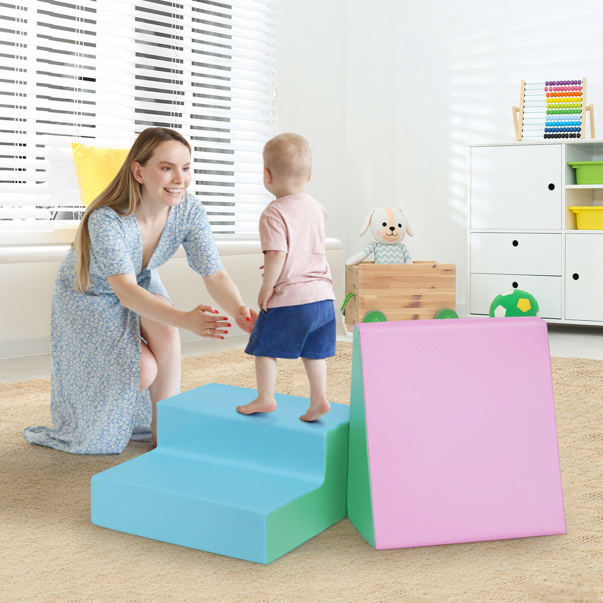 Woman helping a toddler climb the blue steps of the soft play set