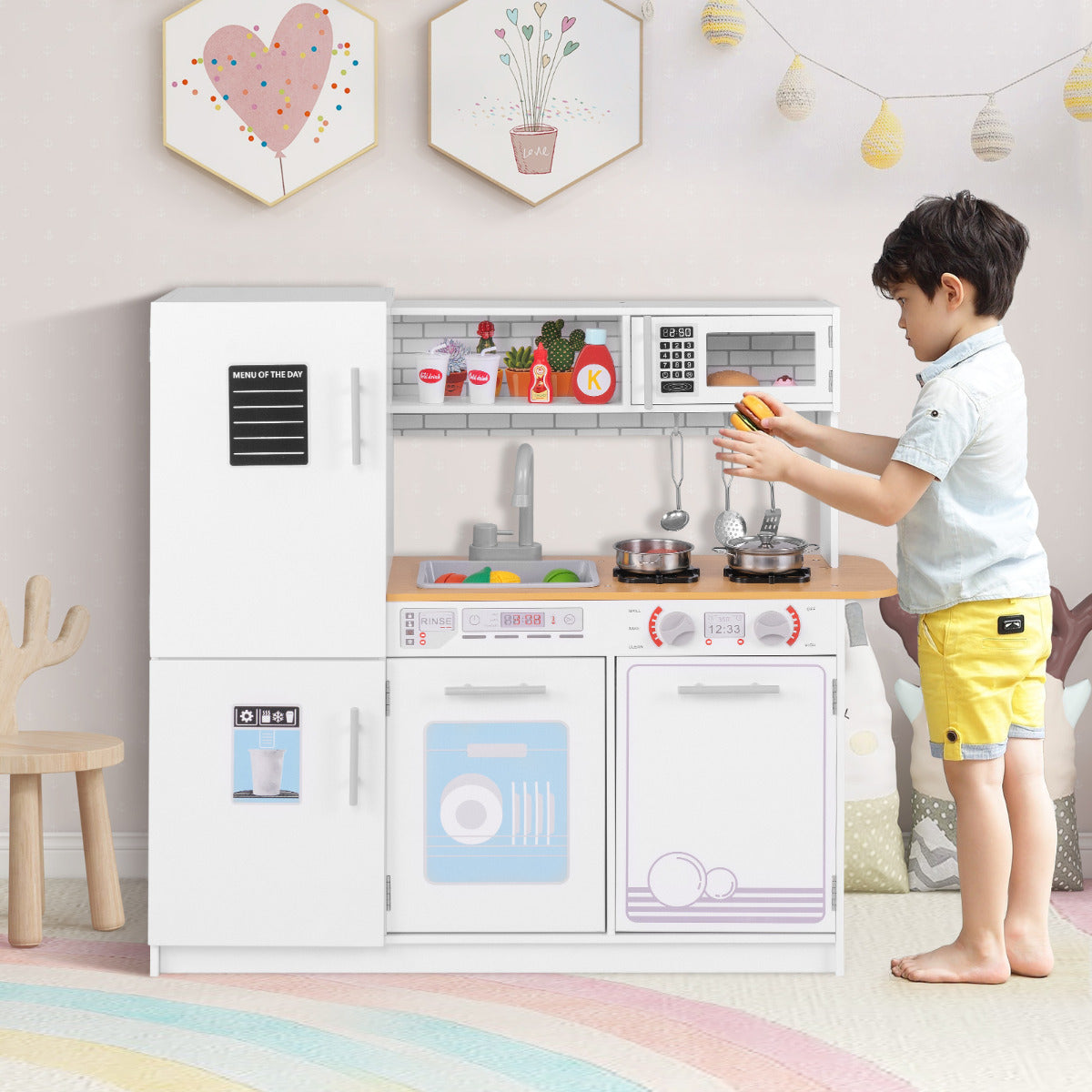 A young boy plays with the white play kitchen set, pretending to cook at the stove