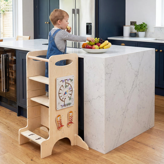 Wooden kids standing tower in use in a modern kitchen, a toddler stands at the counter eating fruit