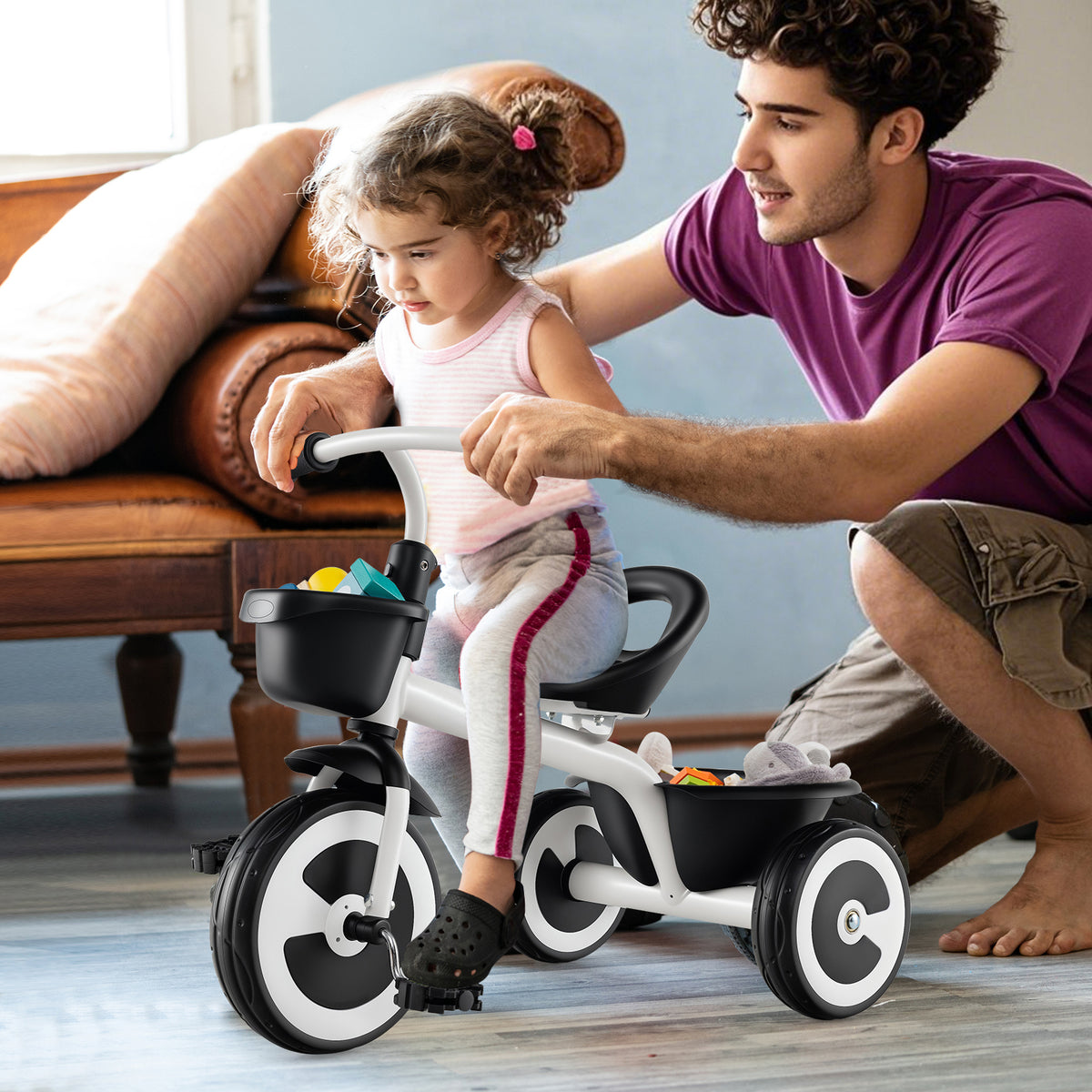 A father pushes his daughter on the white kids trike indoors