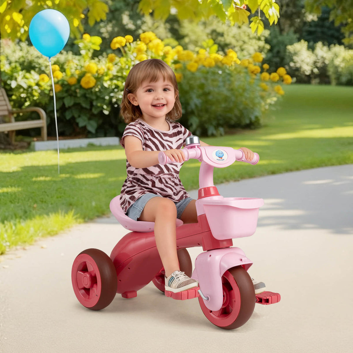 The pink ride on toy with a bell and basket on a paved path in a garden