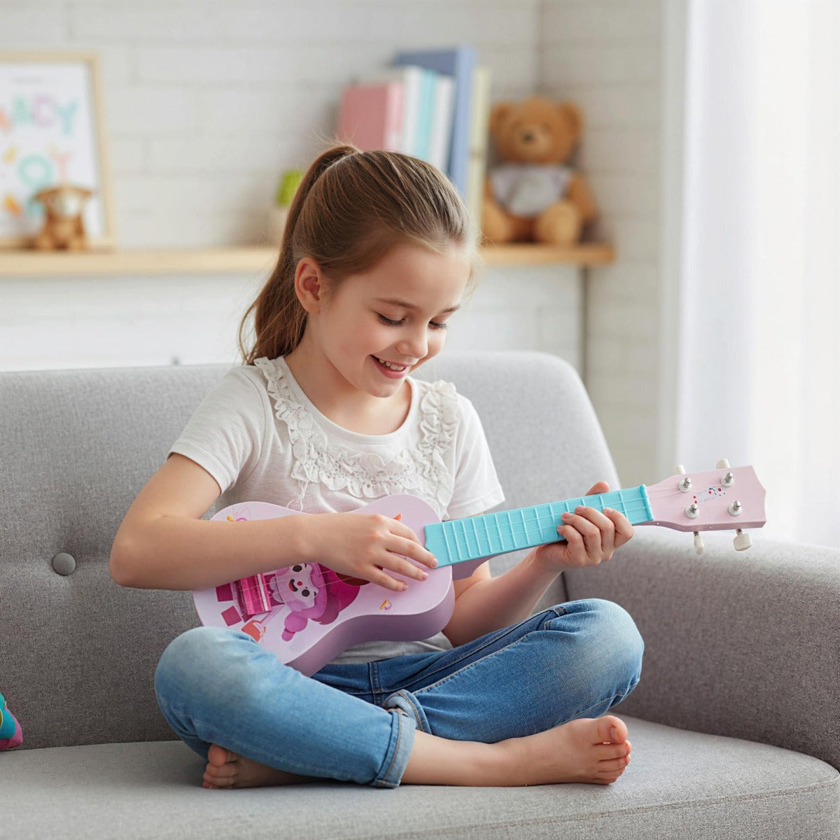 A girl sits on a grey sofa playing the toddler ukulele with a smile