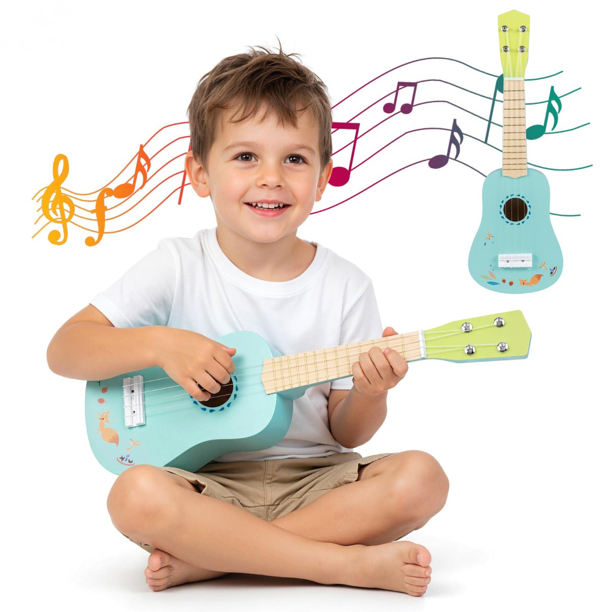A happy young boy sitting on the floor, strumming a light blue toy ukulele with a natural wood neck