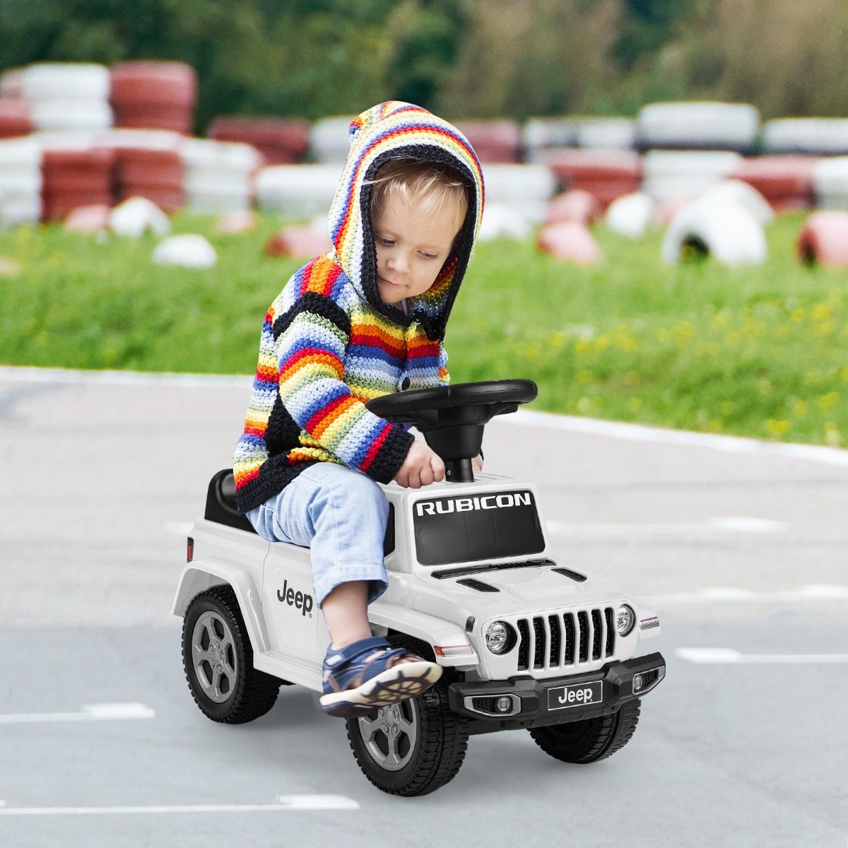 A toddler wearing a colourful hooded jumper sits on the white ride on push car