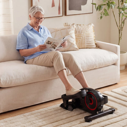 An older woman using the under desk elliptical pedal exerciser while relaxing on a sofa