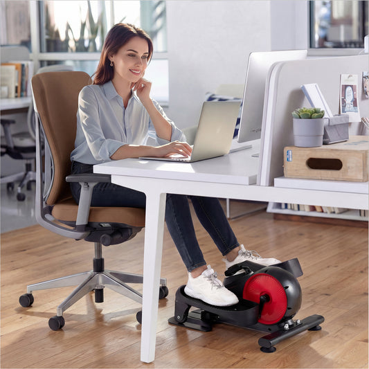 The sport equipment placed under a desk while a woman works on her laptop in an office