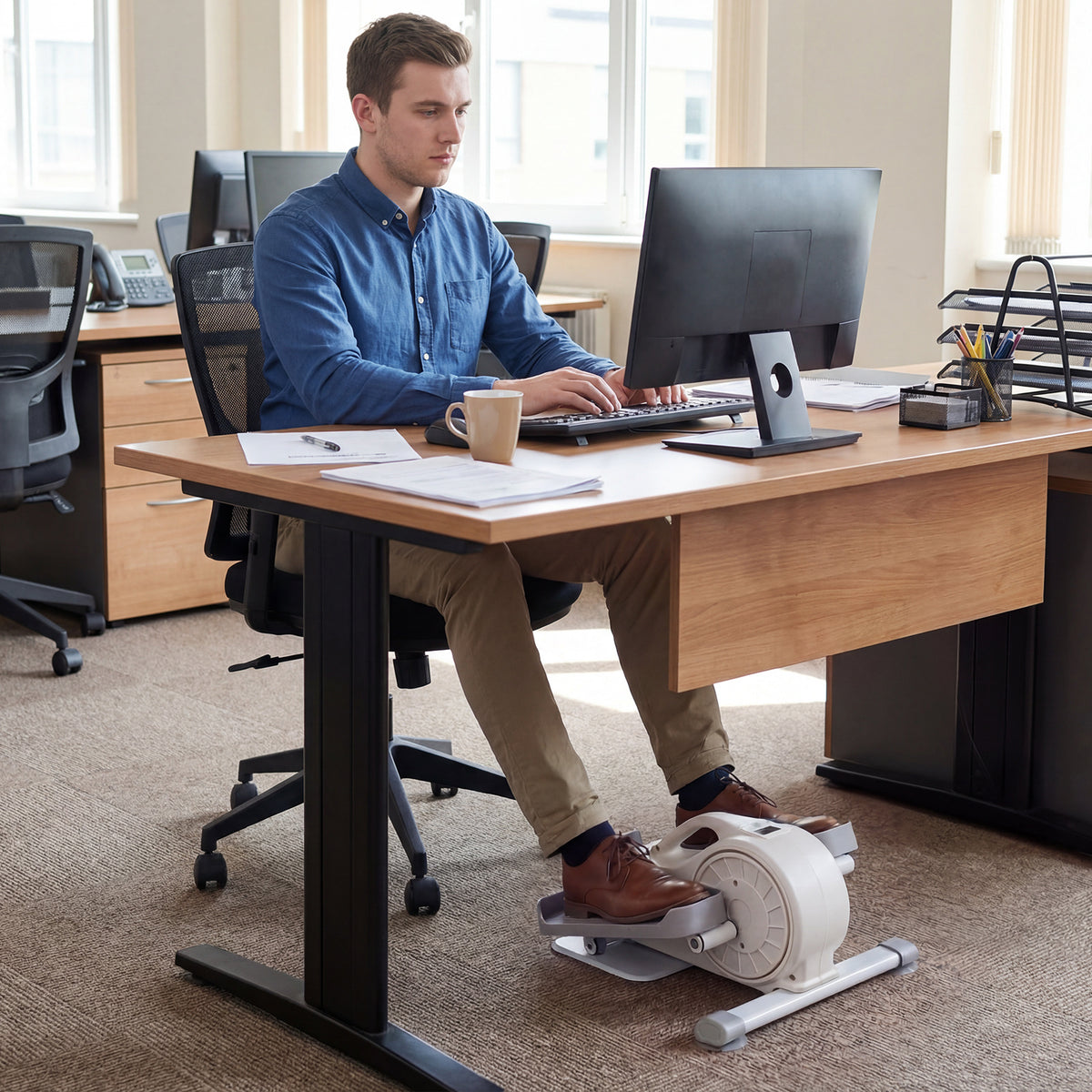 The exercise bike placed under a desk while a man uses it during his work at a computer