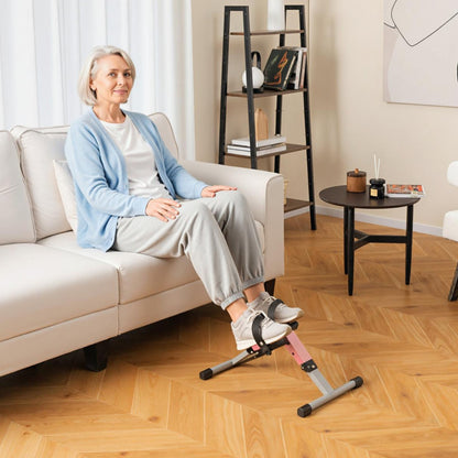 The exercise bike being used by an older woman sitting comfortably on a sofa