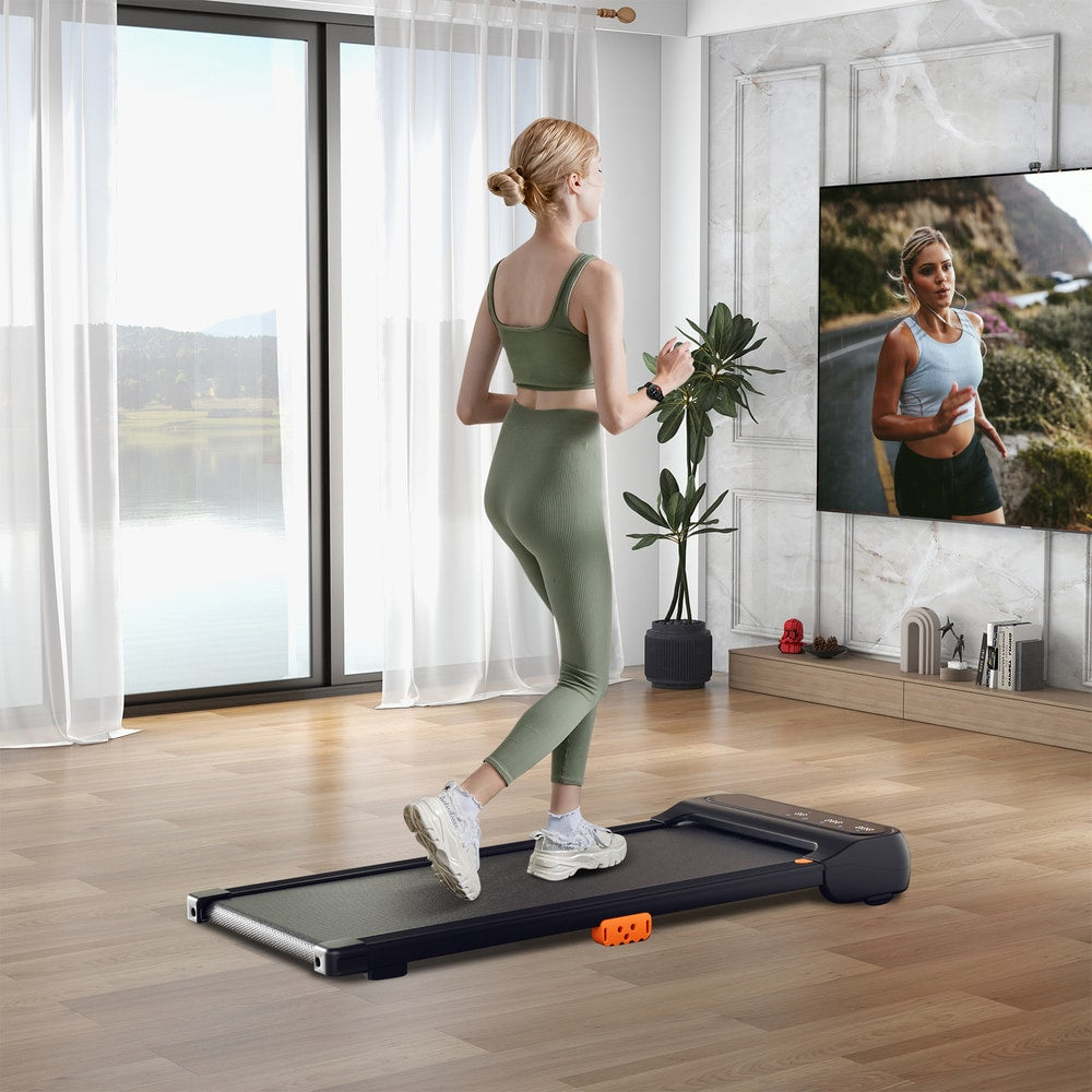 A slim walking treadmill in a bright living room with a woman exercising on it
