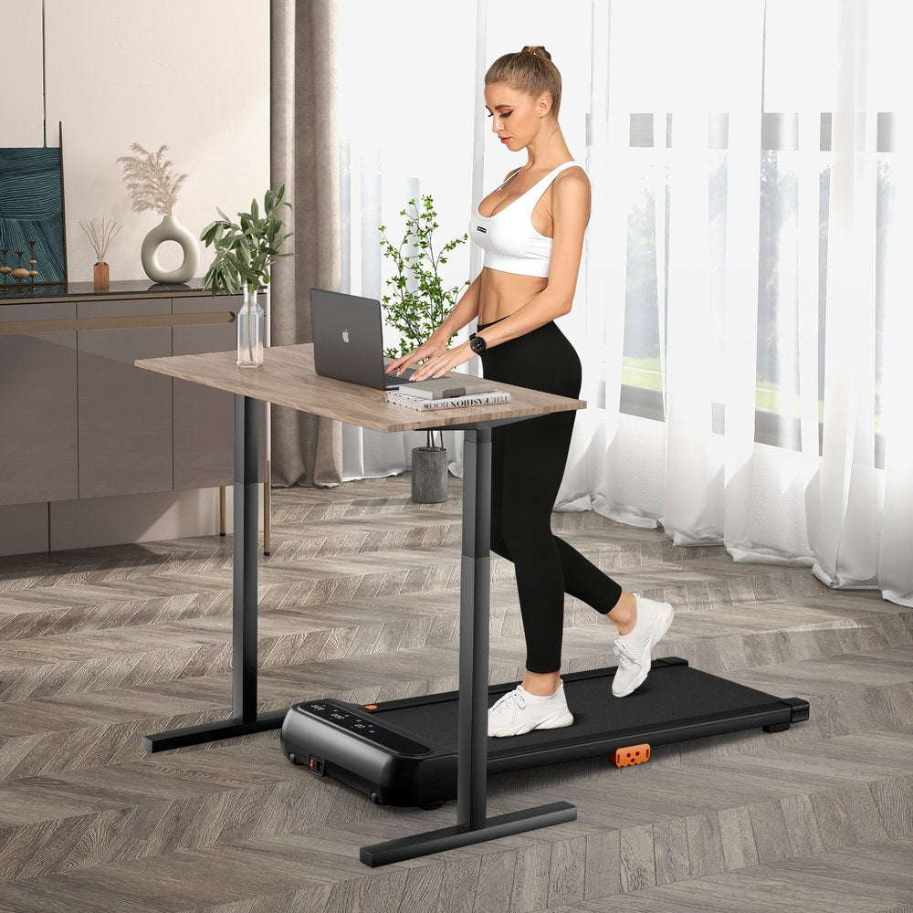 A compact treadmill being used with a standing desk and a woman working on her laptop