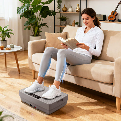 A woman reads a book while sitting on a sofa with her feet on the grey vibration plate exercise machine