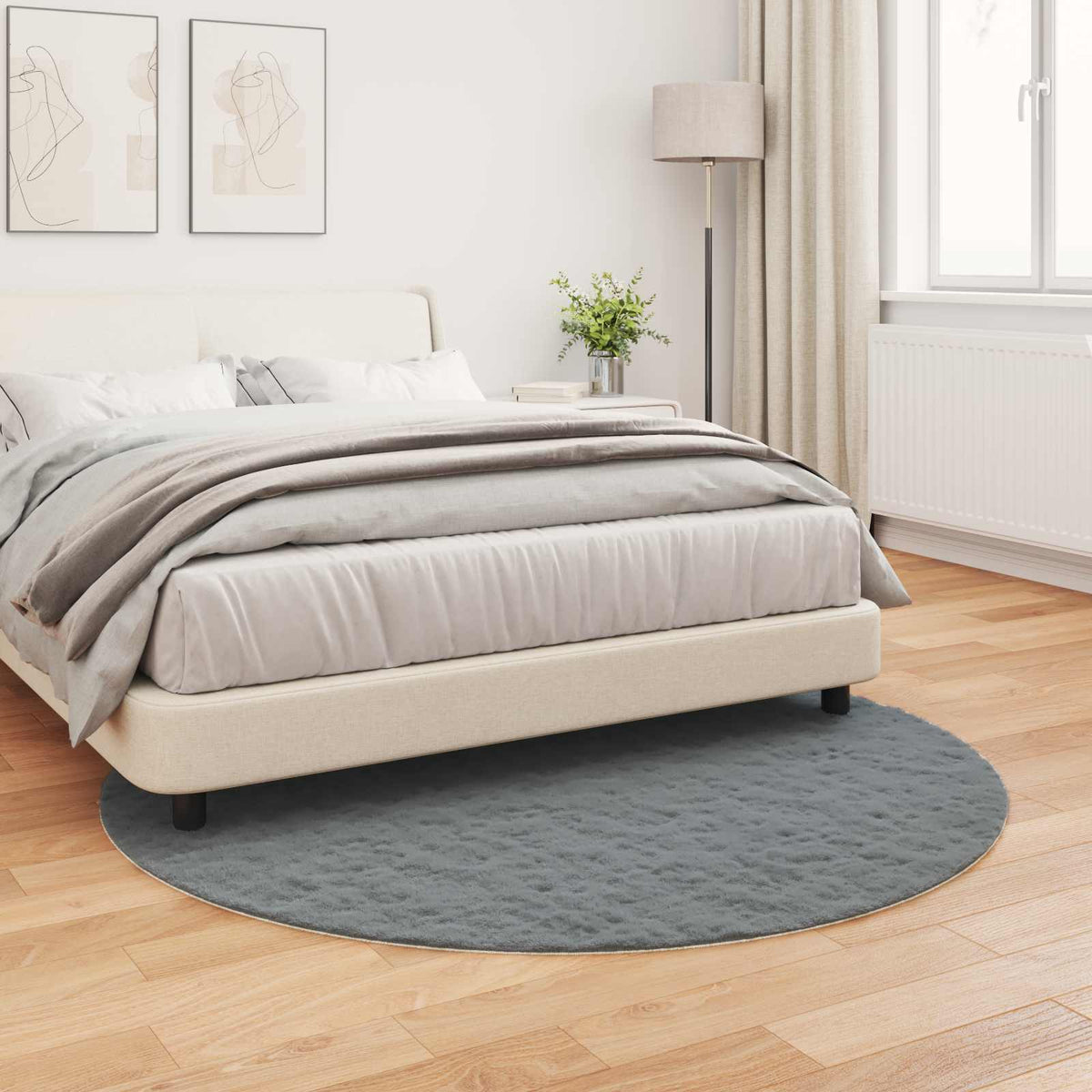 Anti-Slip Faux Rabbit Fur Rug OLITE Anthracite, the round grey rug placed on a wooden floor beside a bed
