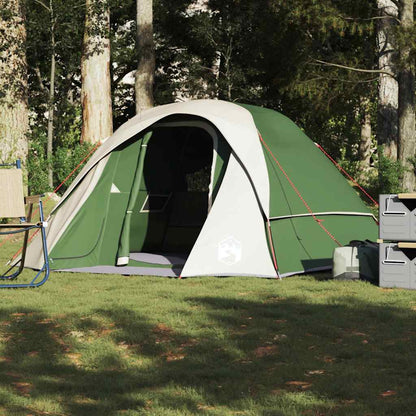 A four-person green camping tent pitched on grass in a woodland setting