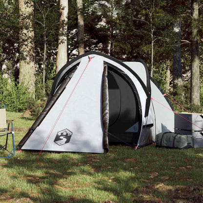 The white two-person camping tent pitched in a woodland setting with camping gear nearby