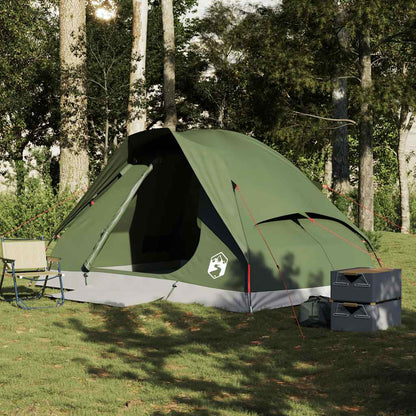 olive green four person camping tent pitched on grass with camping chairs and storage boxes