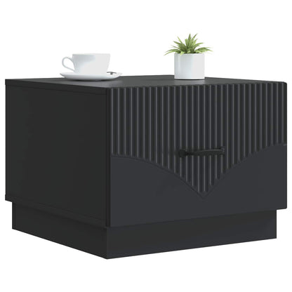 A black engineered wood coffee table with a ribbed front panel and a drawer handle, shown with a cup and plant