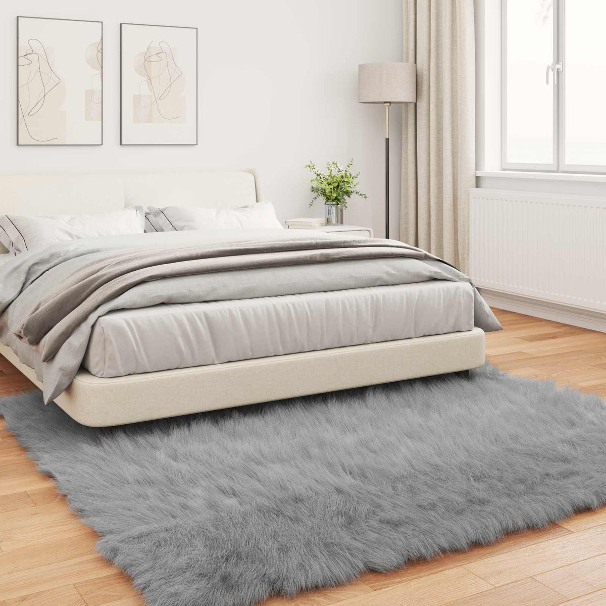 The grey faux sheepskin rug TAFALLA placed on a wooden floor next to a bed