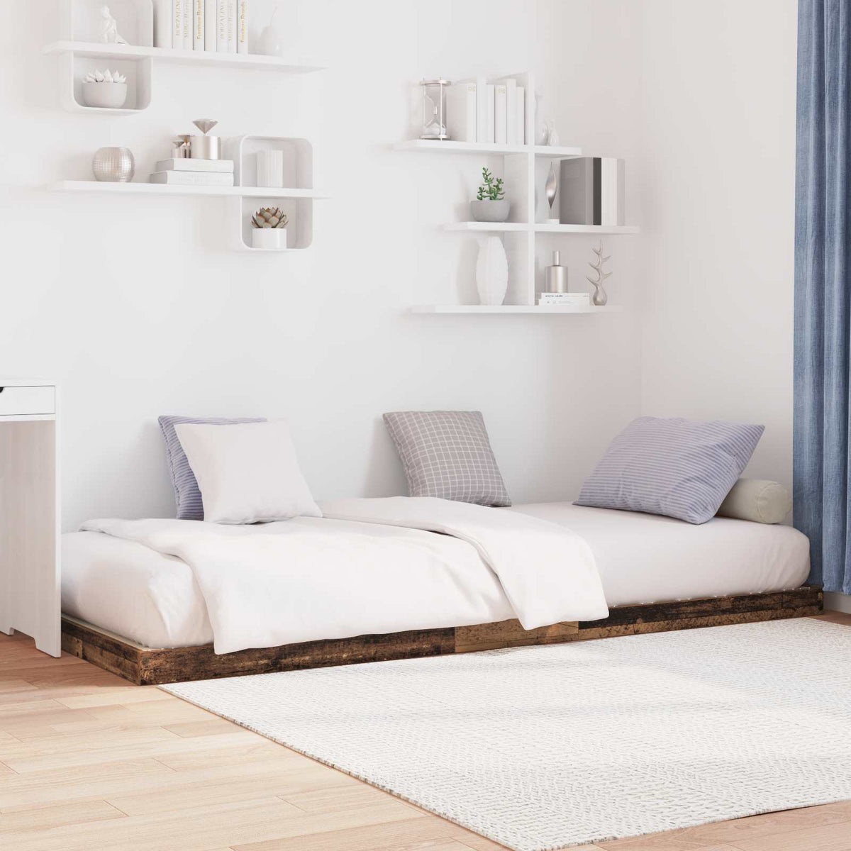 the floor bed frame styled with multiple cushions in a minimalist room with wall shelves
