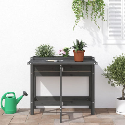 A grey wooden garden planter with a fold-out table set up on a patio with plants and a watering can