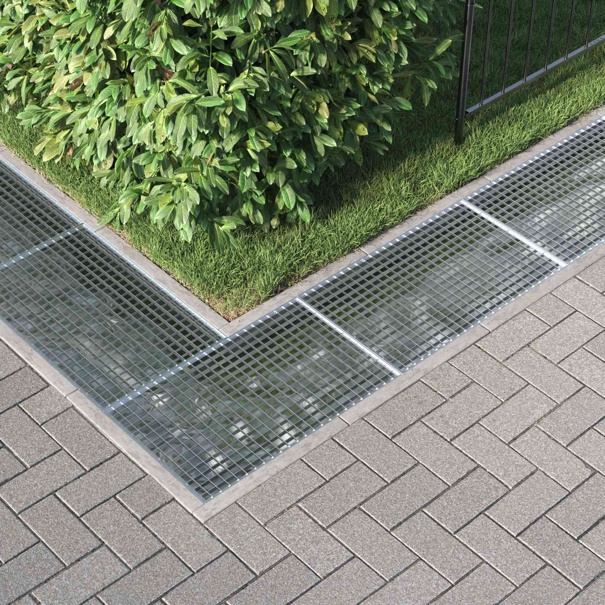 Hot-dip galvanised steel grating drain cover fitted into a paved area with grass and bushes