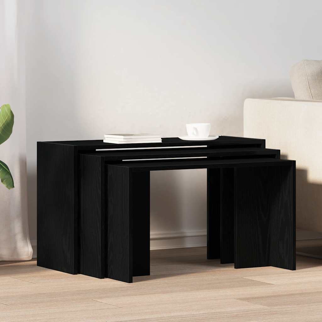Three black nesting tables in a living room setting, one with a cup and book on top