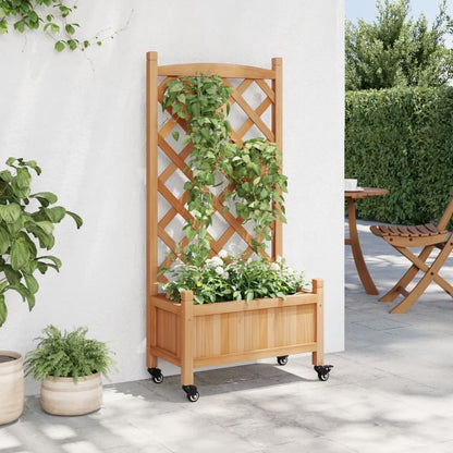 A wooden planter with a trellis and wheels, positioned on a patio next to a white wall and a table