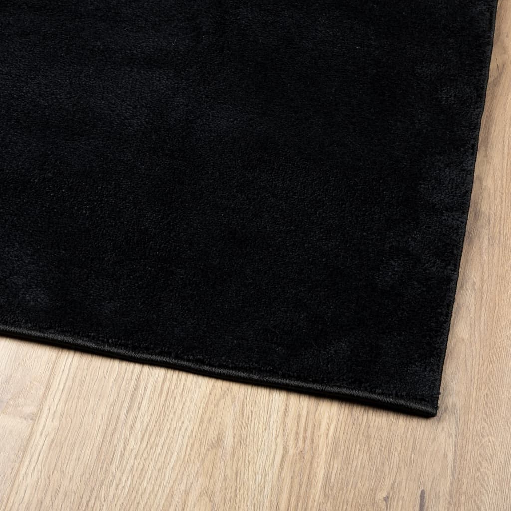 Corner of the black rug showing its short pile texture on wood