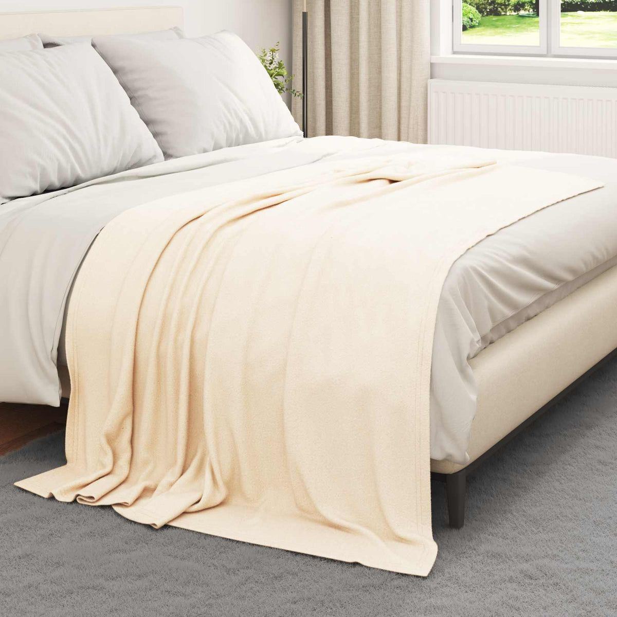 A cream fleece blanket spread across a bed with grey bedding