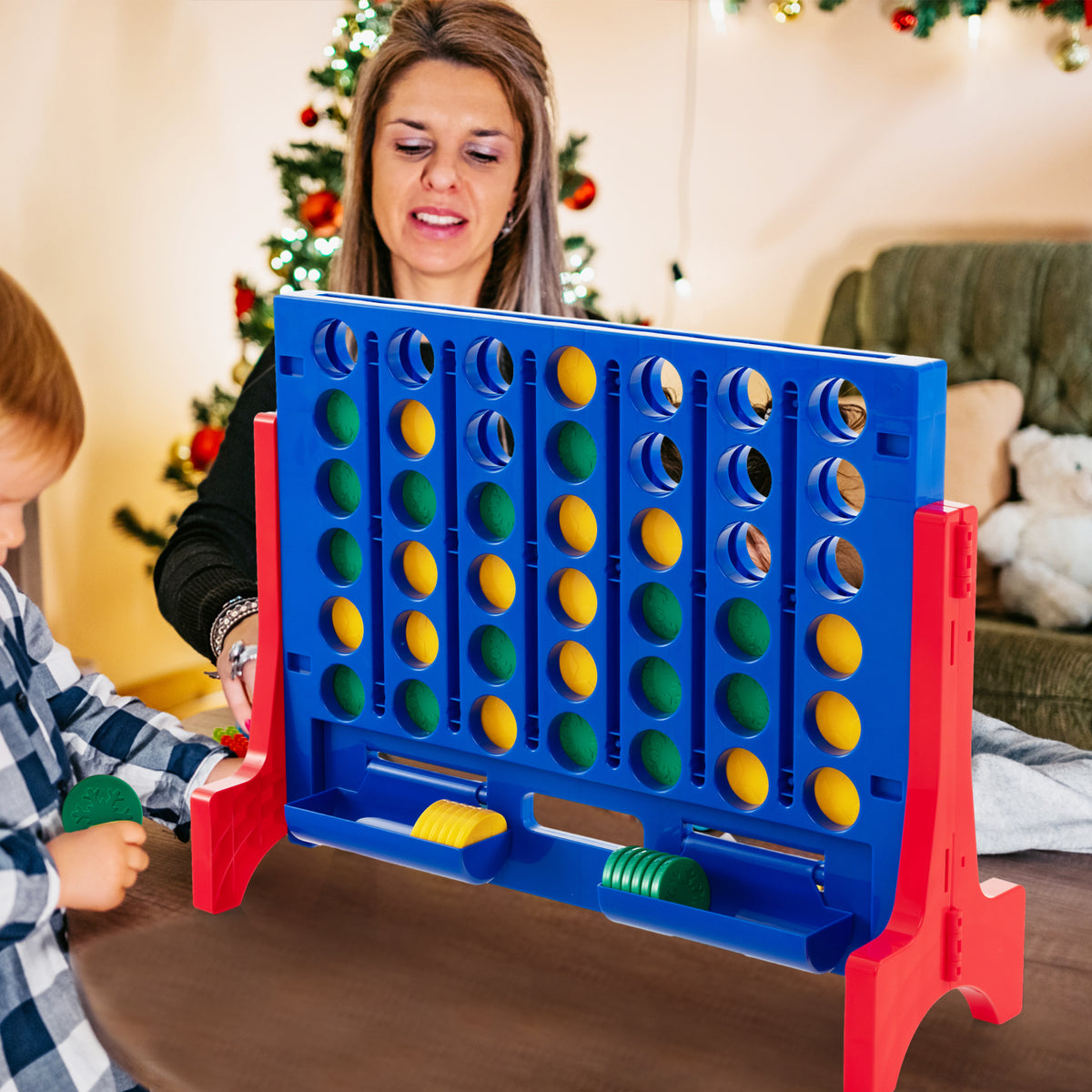 A woman and child playing the giant four-in-a-row lawn game indoors at Christmas