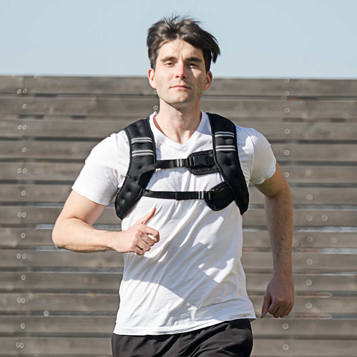 The black fitness vest worn by a man running outdoors against a wooden fence