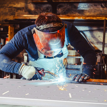 A person wearing a protective welding mask working on metal over the steel workbench surface