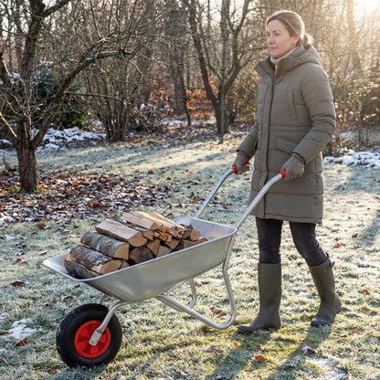 A woman pushing the wheelbarrow cart filled with logs through a frosty garden