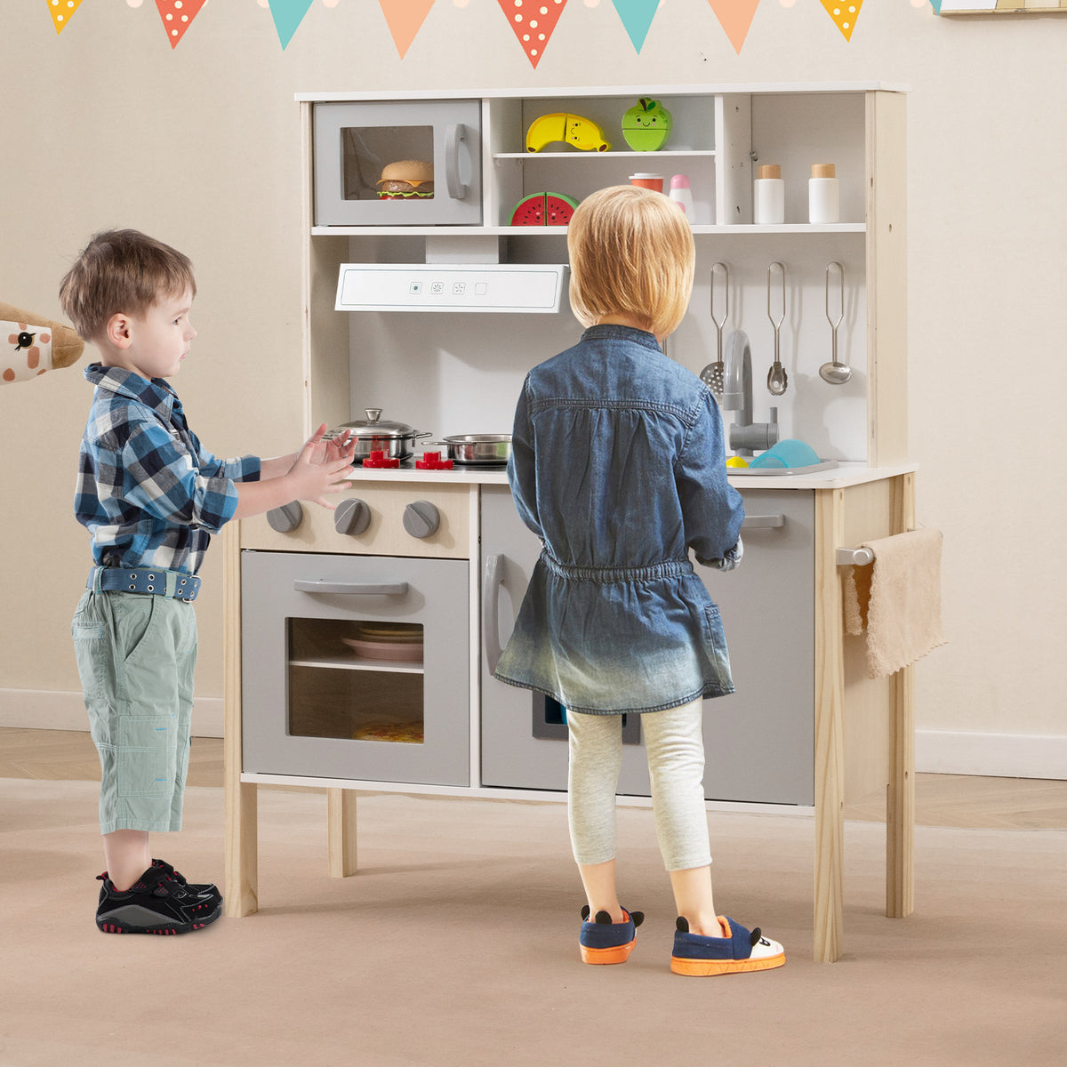 Two children playing with the grey and white wooden play kitchen set in a room