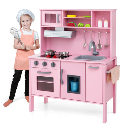 A young girl in an apron and chef's hat stands next to the pink wooden play kitchen set