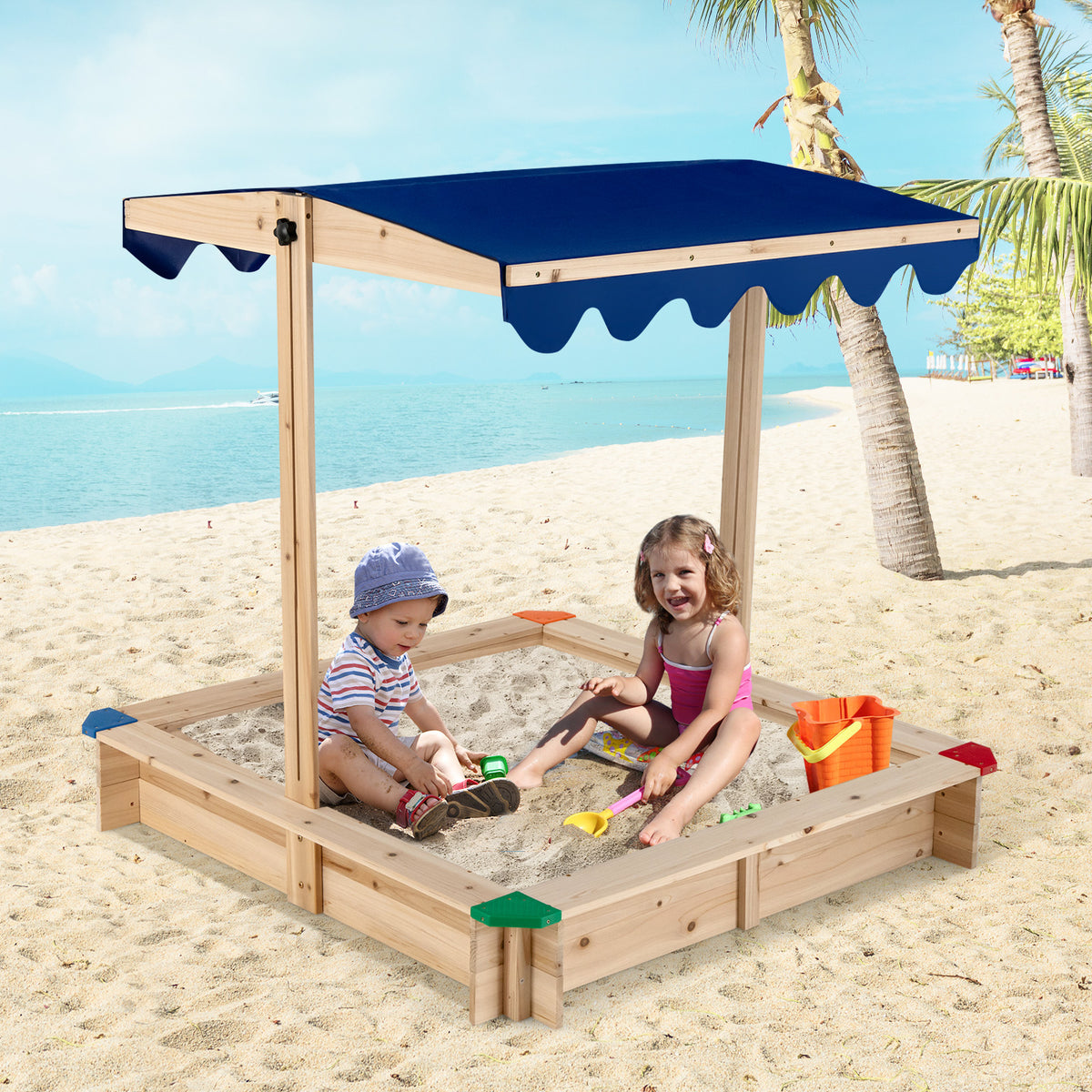 Two children playing in the wooden sandbox on a beach with the blue canopy providing shade